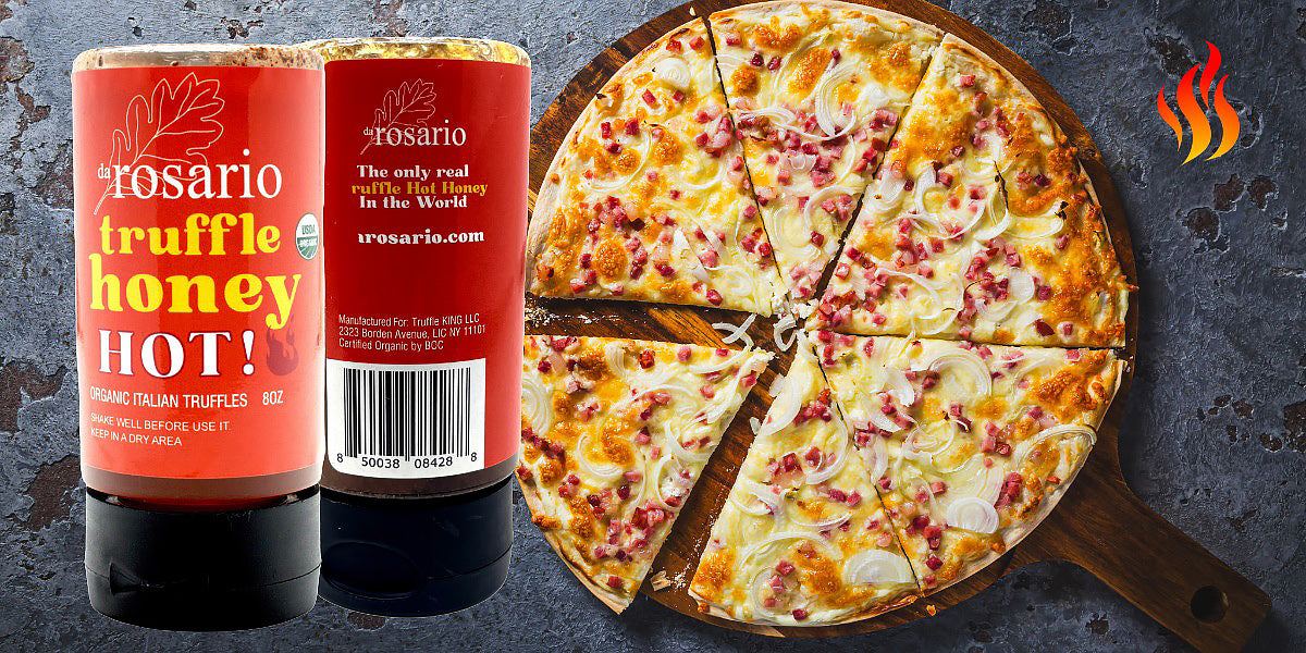 Two bottles of Rosario truffle honey hot sauce next to a pizza on a dark surface.