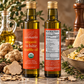 Two bottles of daRosario organic white truffle oil standing on a rustic stone surface with truffles, parsley, pasta, and cheese props. The front bottle shows the orange label with product name and USDA Organic seal, while the rear bottle shows the nutrition facts panel.