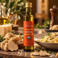 A bottle of daRosario Organic White Truffle Oil stands on a rustic countertop surrounded by sliced white truffles, cheese, pasta, and herbs in a warm, softly blurred kitchen setting.