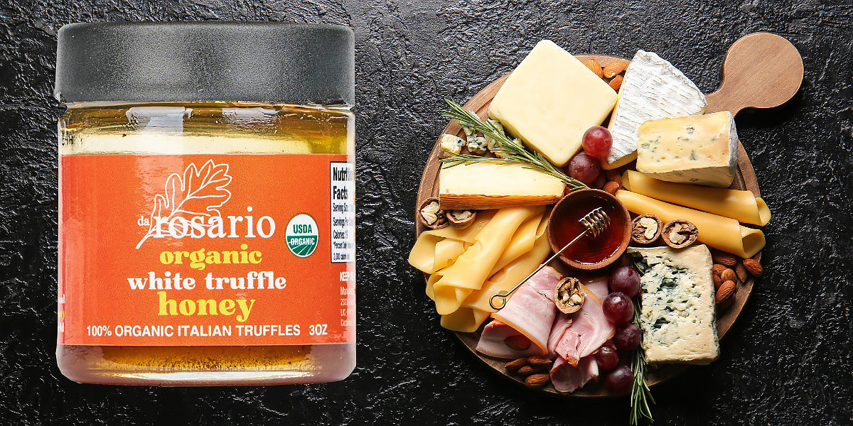 Jar of Rosario organic white truffle honey next to a charcuterie board on a dark surface